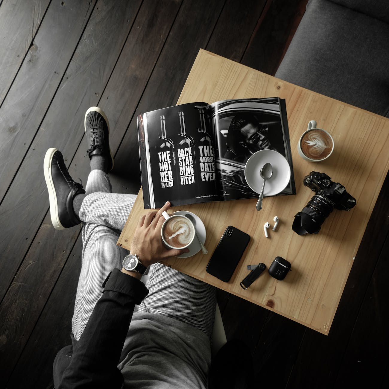 top view of a table with man holding a cup of latte with a magazine camera cellphone and other personal effects